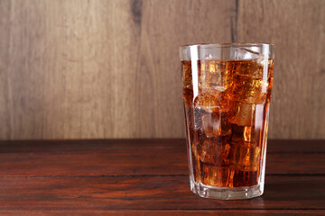 Sweet soda water with ice cubes in glass on wooden table, space for text