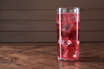 Sweet soda water with ice cubes in glass on wooden table, space for text