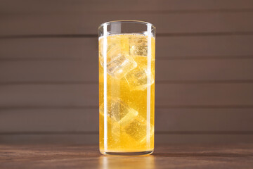 Sweet soda water with ice cubes in glass on wooden table