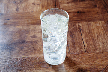 Refreshing soda water with ice cubes in glass on wooden table, closeup