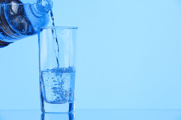 Pouring soda water from bottle into glass on light blue background, closeup. Space for text