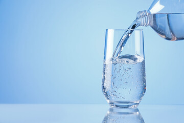 Pouring refreshing soda water from bottle into glass on light blue background, closeup. Space for text