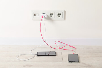 USB adapter with cables plugged into electric socket charging different devices indoors