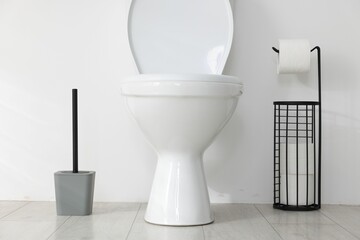 Toilet, brush and necessities near white wall