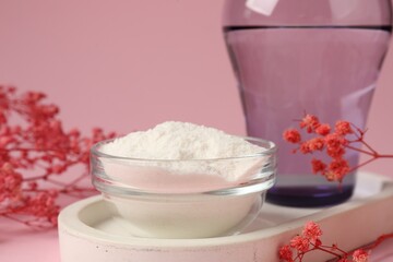 Collagen powder in bowl, glass of water and gypsophila branches on pink background, closeup