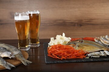 Tasty beer and dried fish snacks on wooden table, closeup