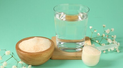 Collagen powder in bowl, scoop, glass of water and gypsophila flowers on turquoise background, closeup
