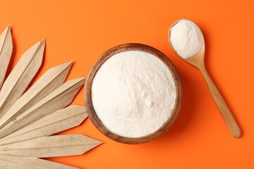 Collagen powder in bowl, spoon and dry palm leaf on orange background, flat lay