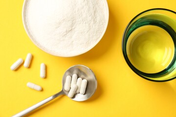 Collagen powder in bowl, spoon with pills and glass of water on yellow background, flat lay