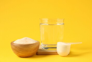 Collagen powder in bowl, scoop and glass of water on yellow background