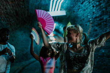 Friends waving colorful fans and dancing at music festival in underground location