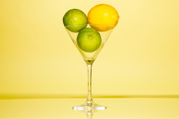 Lemons and limes in martini glass against yellow background