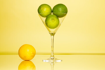 Lemons and limes in martini glass against yellow background