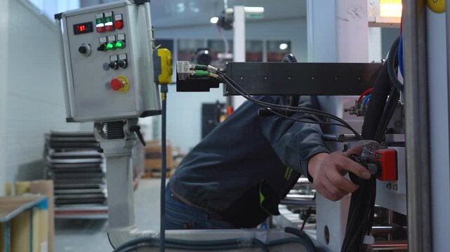 Worker presses stop button on automatic production line at plant closeup. Employee controls work adjusting machine with panel in workshop