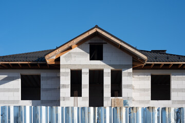 Building under construction with aerated concrete blocks, roof tiles and metal fence on a sunny day with blue sky