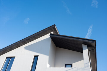 White modern house with black corrugated metal roof against a clear blue sky, representing modern architecture and residential building design
