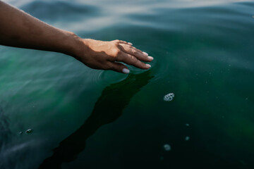 The hand touches the water, creating ripples. The water is calm and clear, and the hand is white. Concept of tranquility and peacefulness.