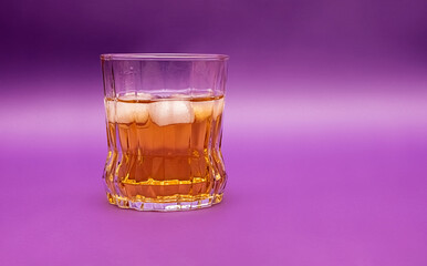 Isolated glass of whiskey sits elegantly against purple backdrop. Filled with ice, reflects light beautifully, creating a warm and inviting atmosphere.