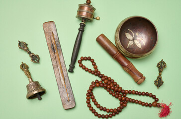 Tibetan singing copper bowl with a wooden clapper on a green background, objects for meditation and...