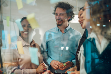Businesspeople planning strategy using adhesive notes on transparent board