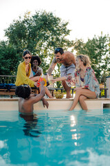 Friends toasting drinks at the poolside during summer party