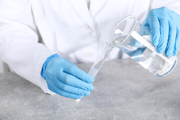 Laboratory testing. Scientist pouring liquid into test tube at grey table indoors, closeup