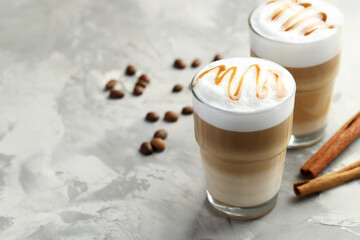 Tasty latte macchiato in glasses, coffee beans and cinnamon on grey table, closeup. Space for text