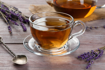 Aromatic lavender tea in glass cup, spoon and dry flowers on wooden table, closeup