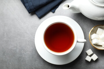 Refreshing black tea in cup, sugar cubes and teapot on grey textured table, flat lay. Space for text