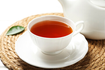 Aromatic black tea in cup and teapot on white table, closeup