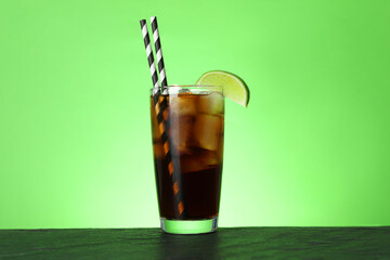Refreshing iced cola with lime slice on black table against green background