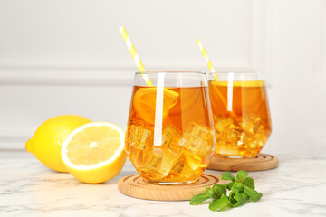 Refreshing iced tea with slices of lemon, mint and drinking straws on white marble table, closeup