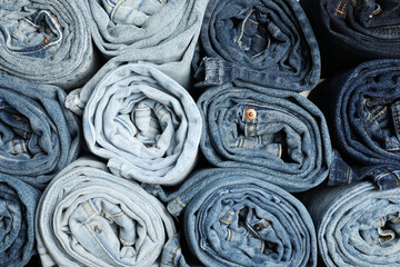Different stylish rolled jeans as background, top view