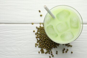 Fresh mung bean juice with ice in glass and seeds on white wooden table, flat lay. Space for text