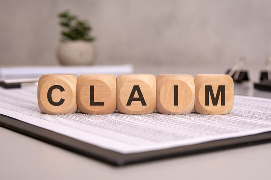 wooden blocks spelling "CLAIM" on documents, symbolizing insurance, legal, and financial claims
