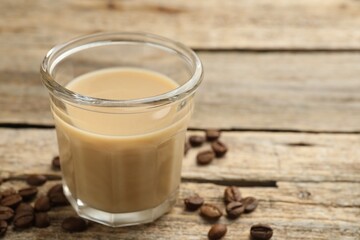Coffee cream liqueur in glass and beans on wooden table, closeup. Space for text