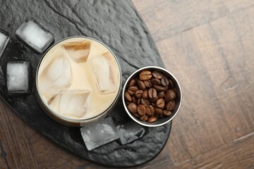 Coffee cream liqueur in glass, ice cubes and beans on wooden table, top view. Space for text
