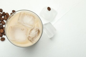Coffee cream liqueur in glass, ice and beans on white table, flat lay. Space for text