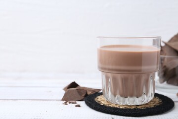 Tasty chocolate milk in glass and pieces of chocolate on white wooden table, closeup. Space for text