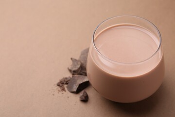 Tasty chocolate milk in glass and pieces of chocolate on brown background, closeup. Space for text
