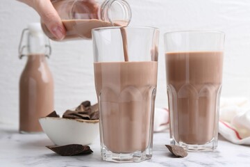 Woman pouring tasty chocolate milk into glass at white marble table, closeup