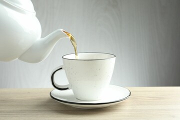 Pouring freshly brewed tea from teapot into cup at wooden table, closeup