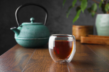 Freshly brewed tea in glass cup and teapot on wooden table