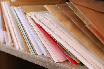 Different paper envelopes on wooden shelf in post office, closeup