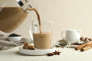Pouring aromatic Masala tea in glass cup at white textured table, closeup