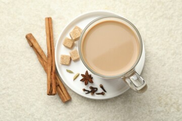 Aromatic Masala tea in glass cup, spices and brown sugar on white textured table, flat lay