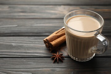 Aromatic Masala tea in glass cup and spices on wooden table, closeup. Space for text