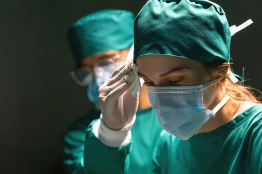 staff support tired surgeon wipe sweat while operating surgery with tissue. doctor trying to help person while nurse using cotton to remove wet face. professional team support operation saving person