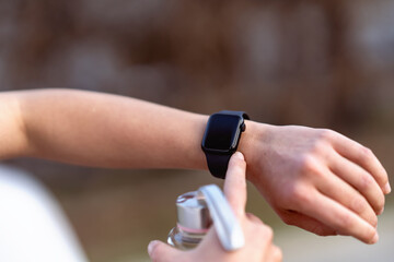 Close-up of a person&rsquo;s hand wearing a black smartwatch while holding a water bottle, touching the screen to check fitness data, with a blurred outdoor background.