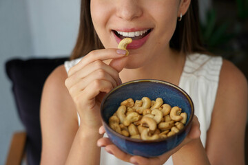 Cashew nuts. Unidentified young woman eating cashew nuts as snack at home.
